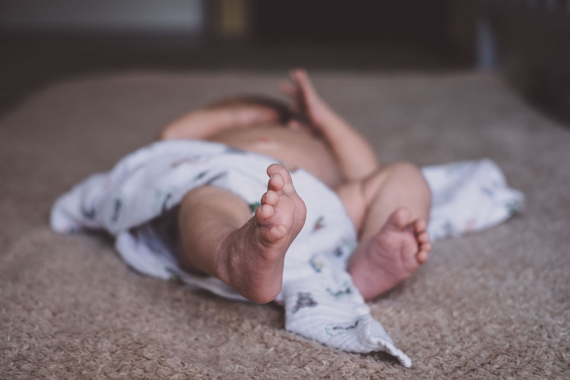 A peaceful baby sleeping on the floor wrapped in a soft blanket indoors.