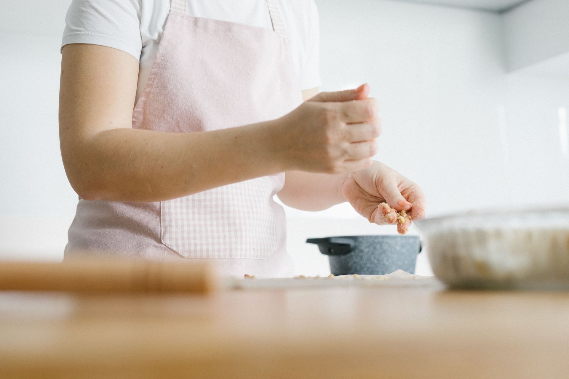 Woman in a pink apron prepares food in a bright kitchen. Culinary focus.